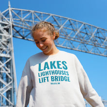 Load image into Gallery viewer, Lakes Lighthouses and Lift Bridge cream sweatshirt in front of the Aerial Lift Bridge
