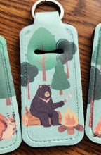 Load image into Gallery viewer, Neopreme chapstick holder keychain with bear roasting marshmallows by a campfire