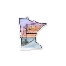 Load image into Gallery viewer, Minnesota shaped sticker that shows watercolor sunrise painting with Duluth's Aerial Lift Bridge