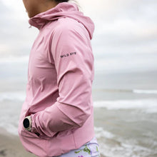 Load image into Gallery viewer, Woman wearing blush windbreaker next to a body of water. Says Wild Rye on the upper arm.