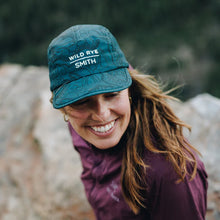 Load image into Gallery viewer, Woman smiling at the camera wearing a teal quick dry Wild Rye and Smith collaboration hat