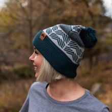 Load image into Gallery viewer, Person wearing a blue and gray patterned beanie with a pom-pom outdoors.