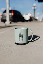 Load image into Gallery viewer, Light blue mug with tree design on a street