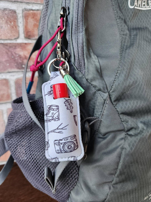 white keychain chapstick holder with hiking and nature icons hooked to a backpack