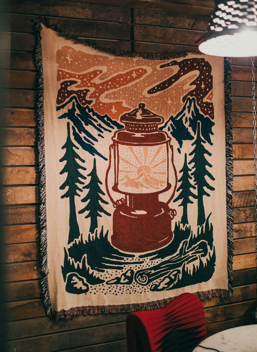 throw blanket with trees, mountains, stars, and lantern hanging on the wall