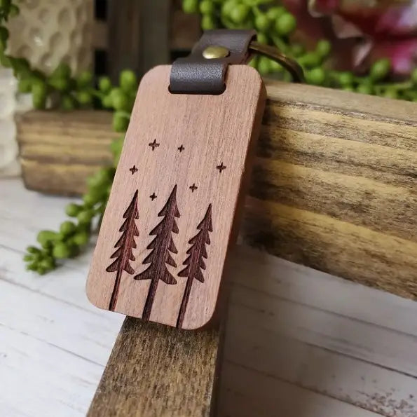 Wood keychain on leather clasp. Wood has three trees and stars engraved.