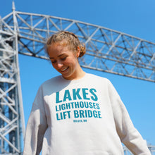 Load image into Gallery viewer, Lakes Lighthouses and Lift Bridge cream sweatshirt in front of the Aerial Lift Bridge
