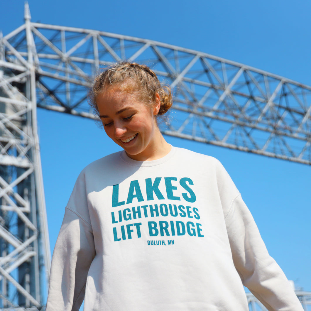 Lakes Lighthouses and Lift Bridge cream sweatshirt in front of the Aerial Lift Bridge