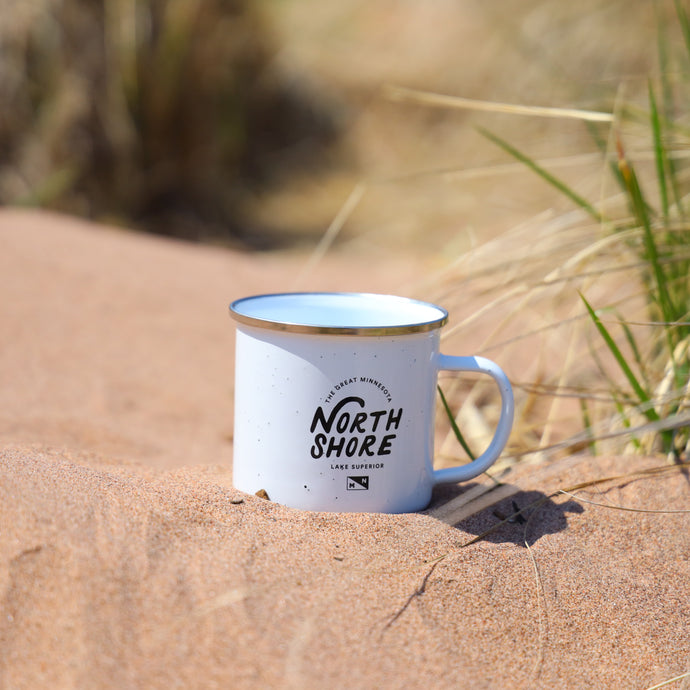 White mug in sand that says the great Minnesota North Shore Lake Superior