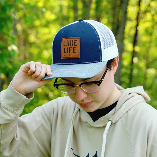 Model wearing blue and white hat with leather patch that says lake life