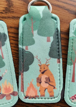 Load image into Gallery viewer, Chapstick holder with a deer warming his hands by a campfire
