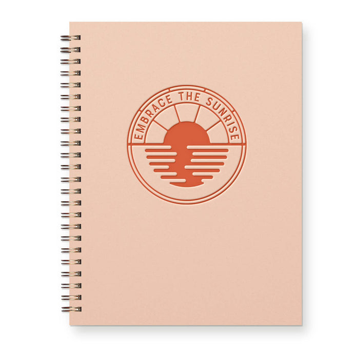 Notebook that is coral with orange logo that says emrbrace the sunrise