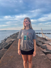 Load image into Gallery viewer, Woman wearing grey tshirt that says the trail awaits you with hiking icons. She is standing on a Lake Superior pier
