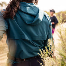 Load image into Gallery viewer, Woman wearing teal windbreaker showing the back and hood
