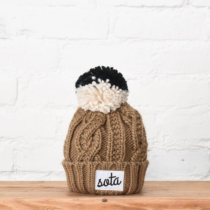 brown knit hat with black and white pom on top and sota patch on the front