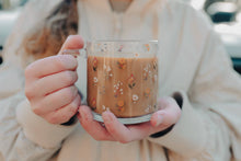 Load image into Gallery viewer, Person holding glass mug of coffee. Glass has wildflowers all over it
