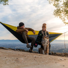 Load image into Gallery viewer, two people on a hammock with a dog sitting by it
