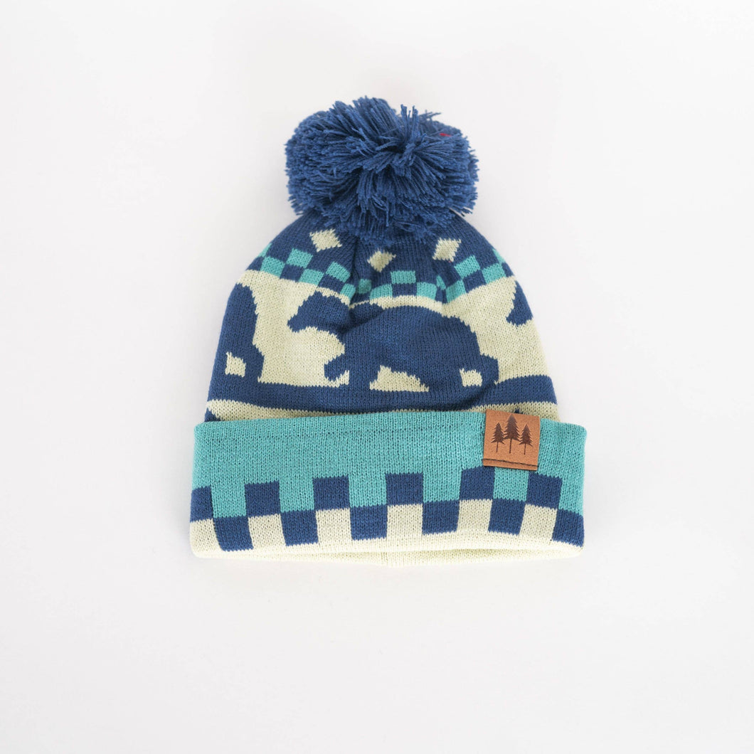 Kid's hat with blue bear and checkered design. Has a pom on the top and leather patch with 3 trees on it.