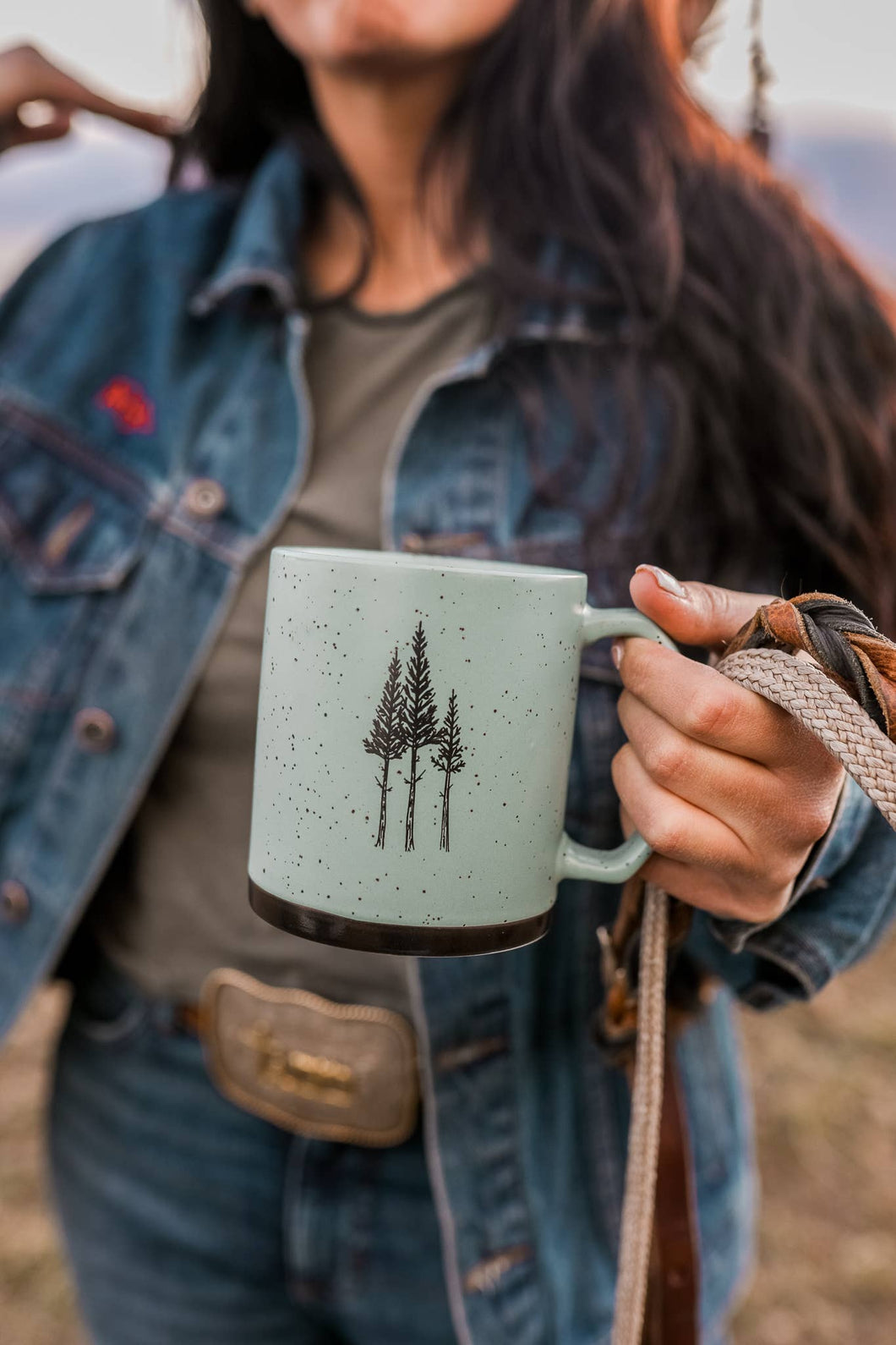 Person holding a mug with tree design outdoors